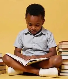 A young KALE student reading a book on the classroom floor